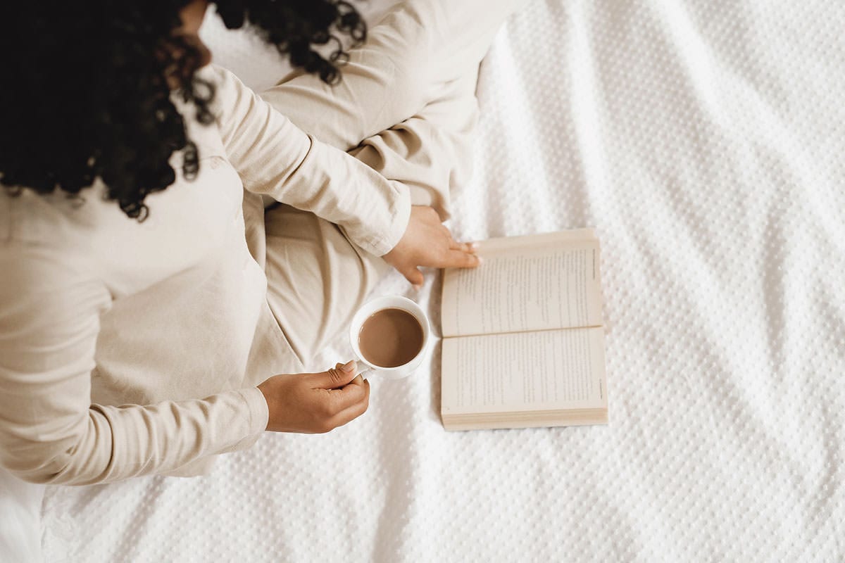 Woman reading a book in bed with a cup of coffee