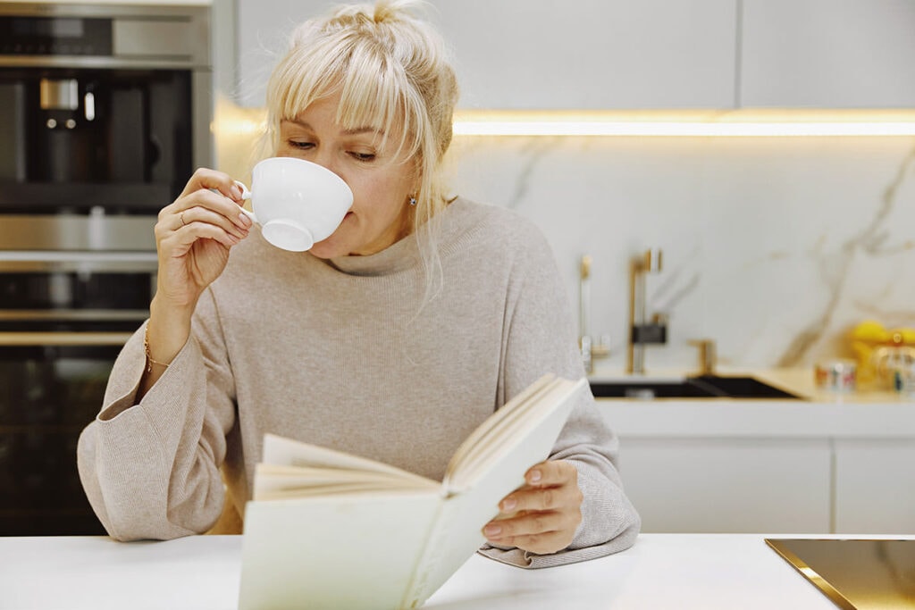 Middle-aged woman reading book and drinking tea at table