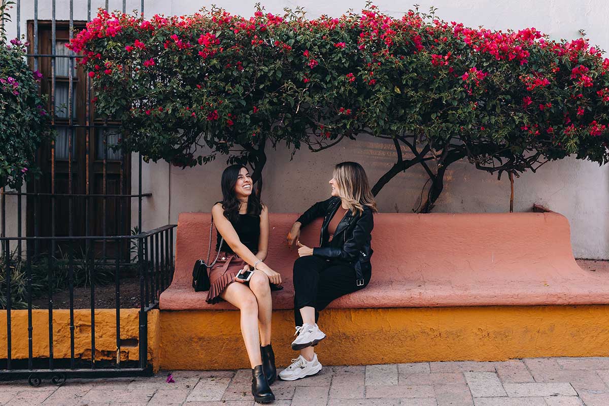 Two female friends chatting on a bench outside