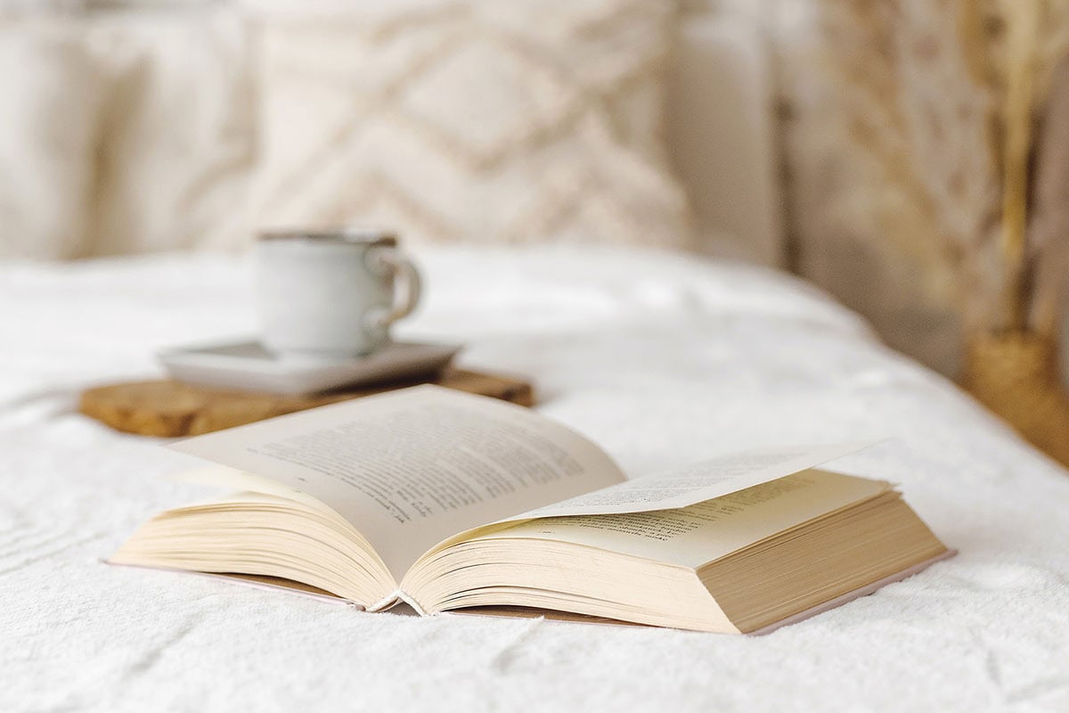 Book and cup of tea laying on a bed