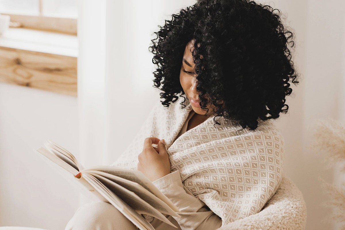 Woman reading in chair wrapped in blanket