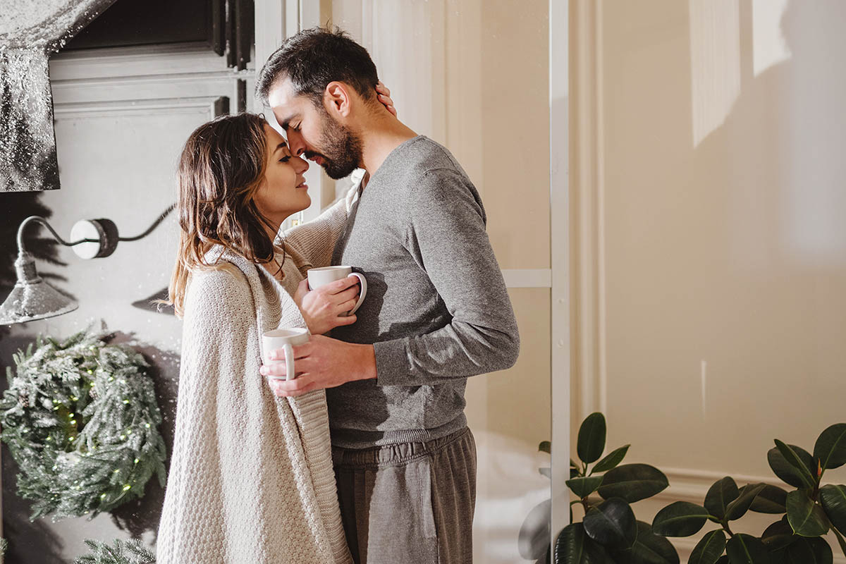 Couple snuggling standing up with coffee mugs