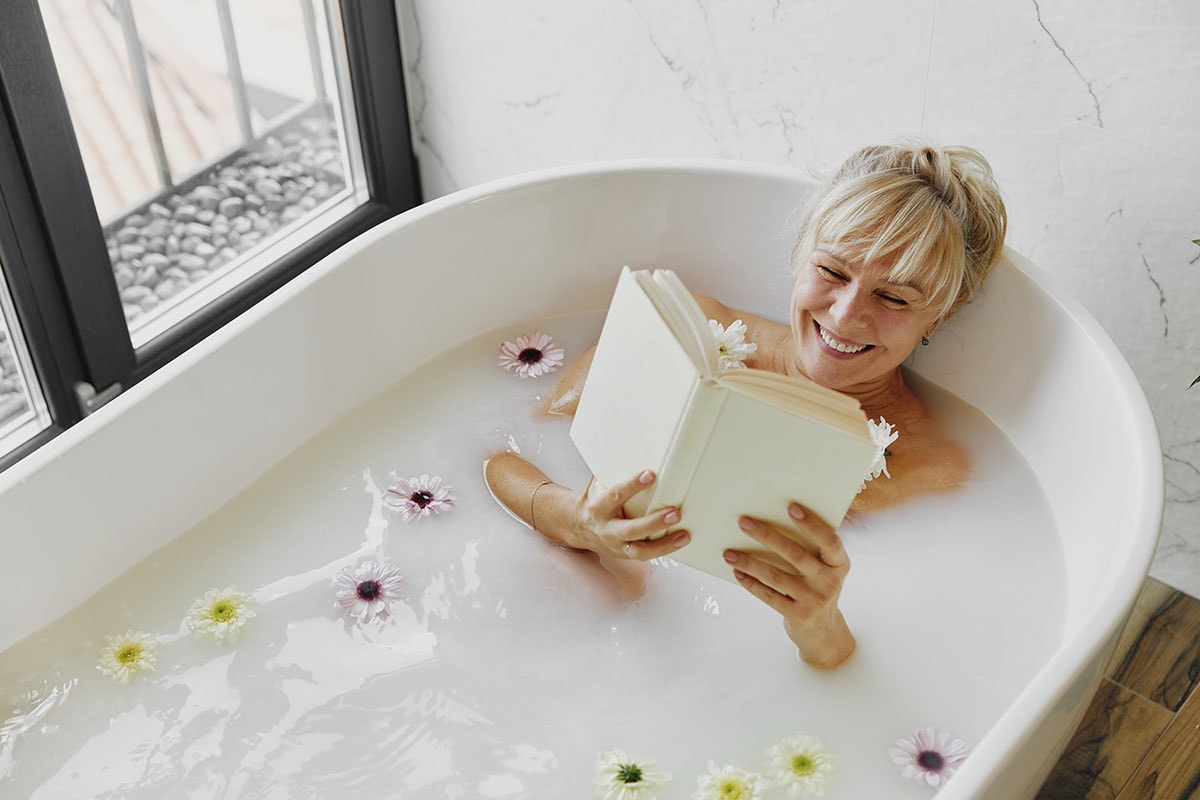 Middle aged woman smiling and reading in the bath