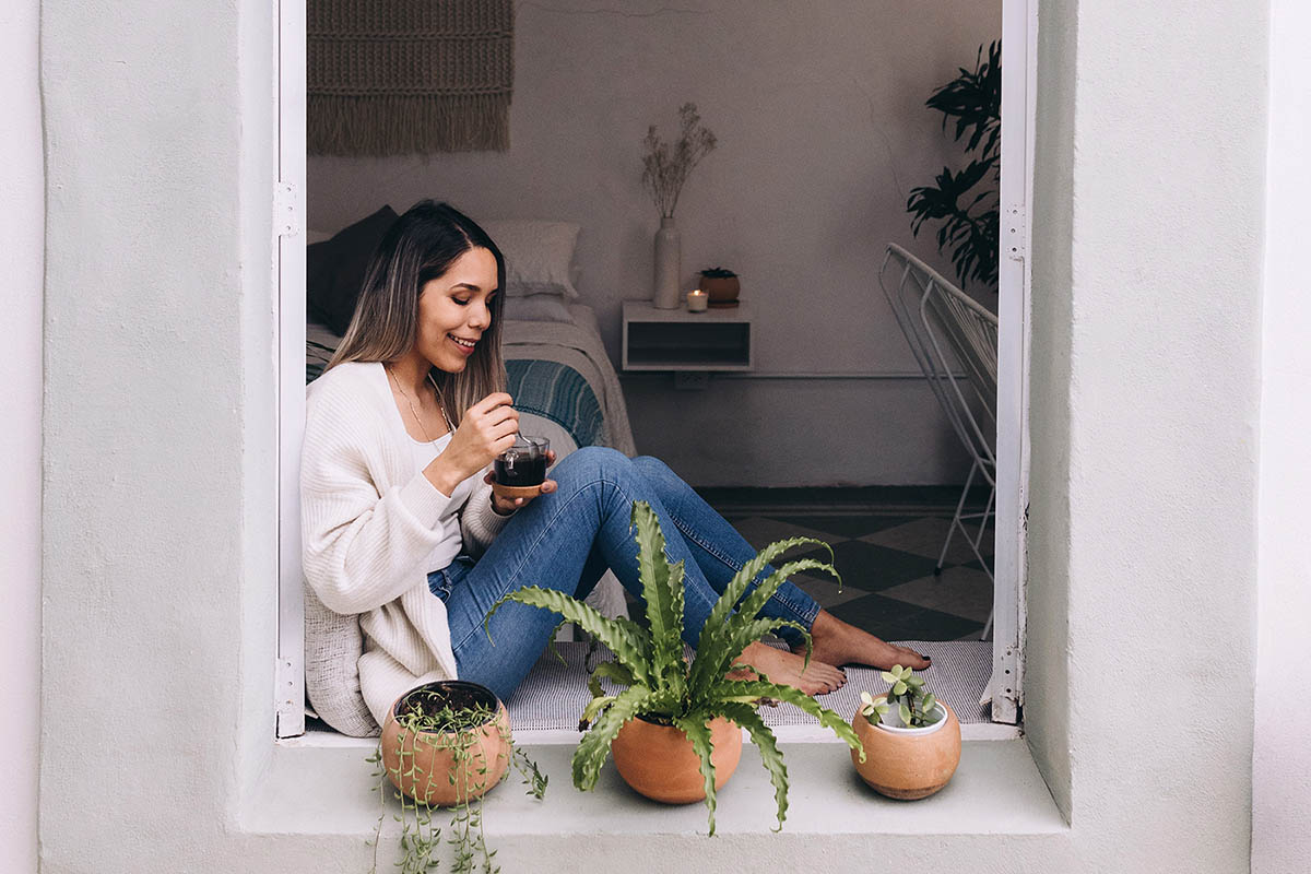 Woman sipping coffee on windowsill with plants
