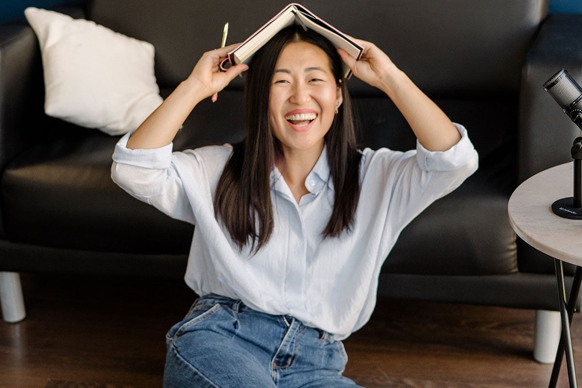 Woman sitting on floor and laughing with book on her head