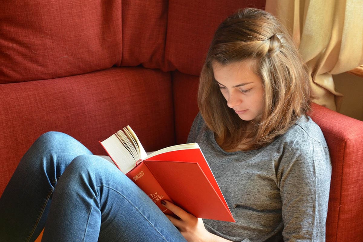 Teen girl reading book on red couch