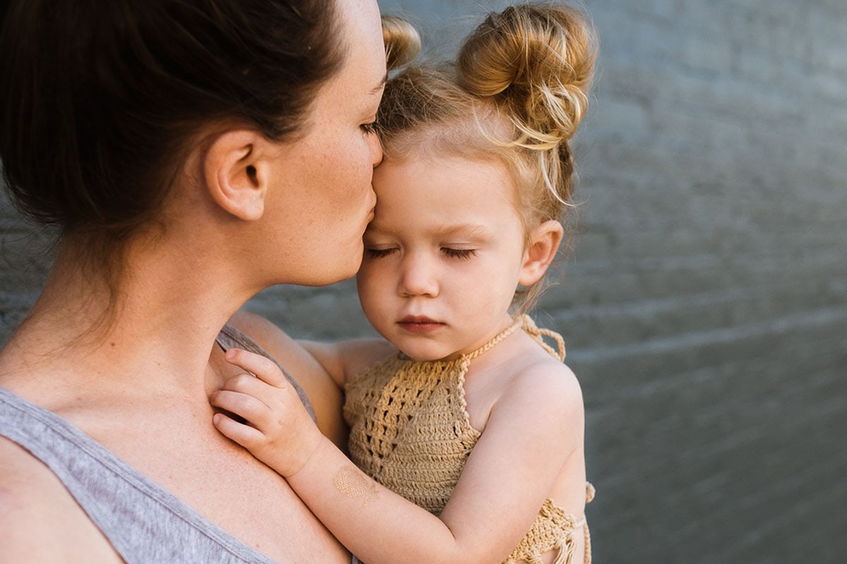 Mother holding a young daughter and kissing her forehead