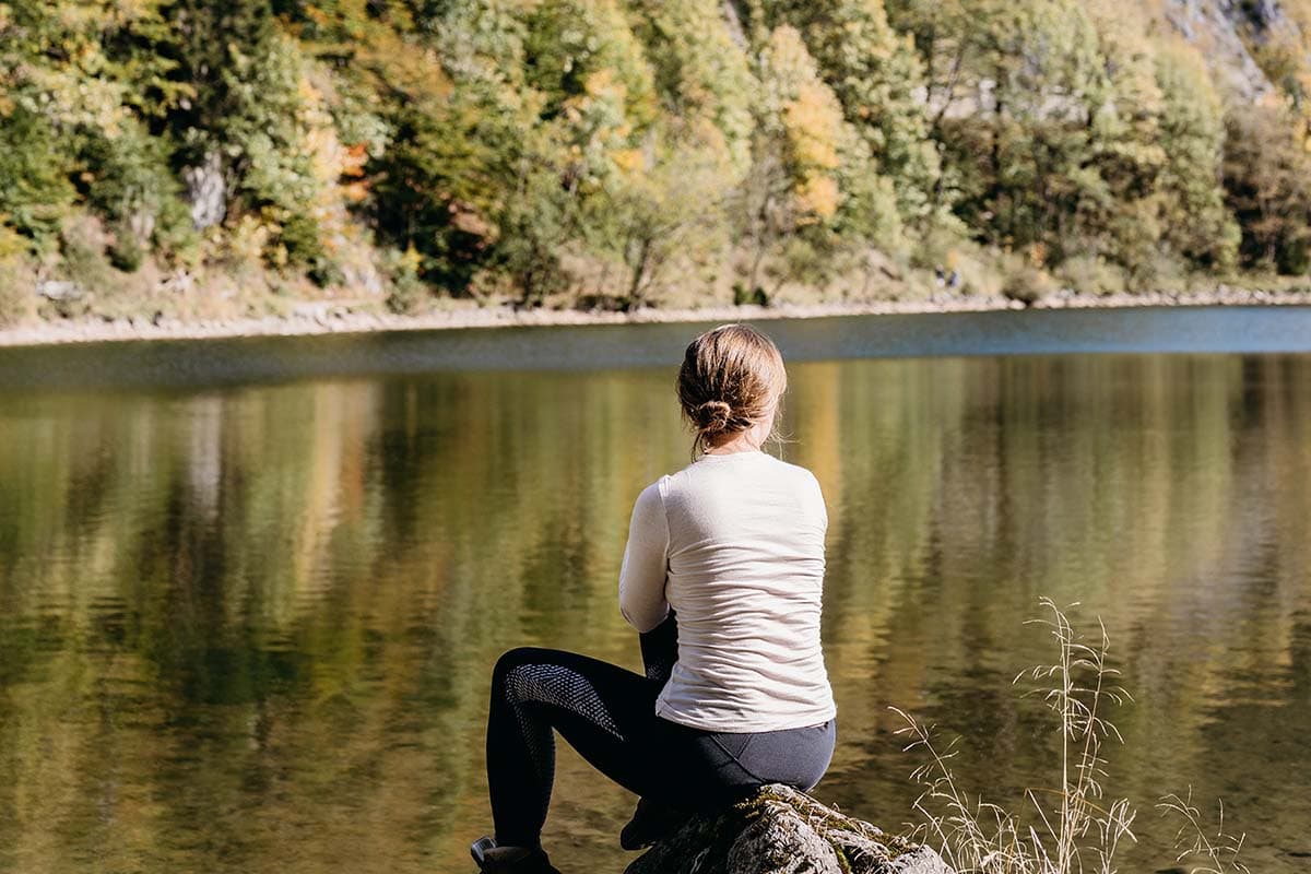 Solo Dates 5 | Woman in hiking gear overlooking a calm wooded lake landscape