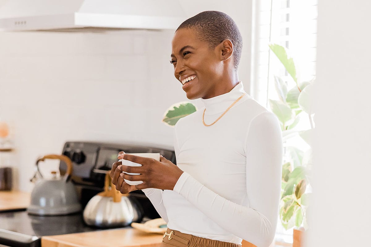 Woman smiling in beautiful kitchen with cup of coffee in hand