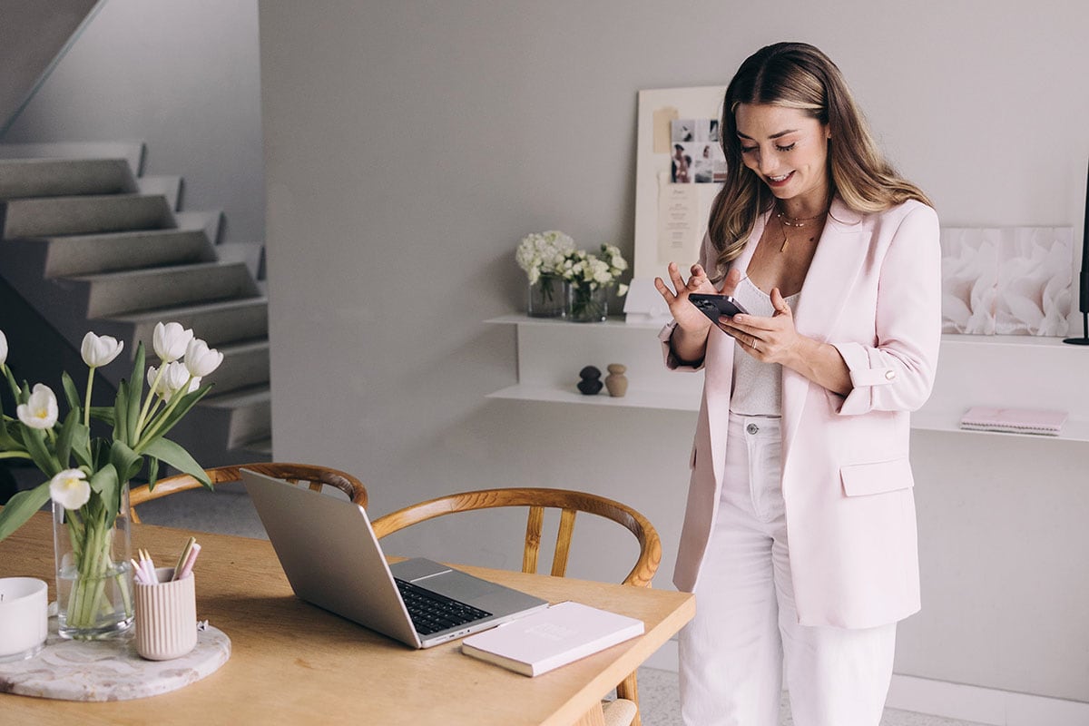 woman with in pink blazer smiling at phone